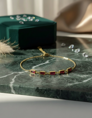 Gold bracelet with red stones on a marble surface with a green box in the background